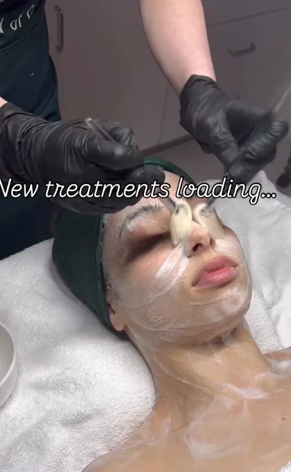 Person lying on a treatment bed receives a facial mask from a gloved professional; text overlay reads, “New treatments loading...”. - Jón Alan Salon in Nashville and Franklin, TN
